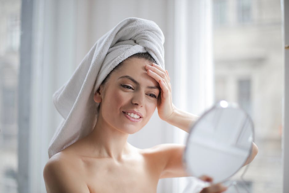 A woman with a towel on her head looking in a handheld mirror and smiling