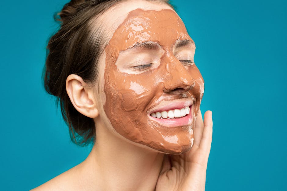 Close-up of a woman smiling with a clay mud mask on her face on a turquoise background
